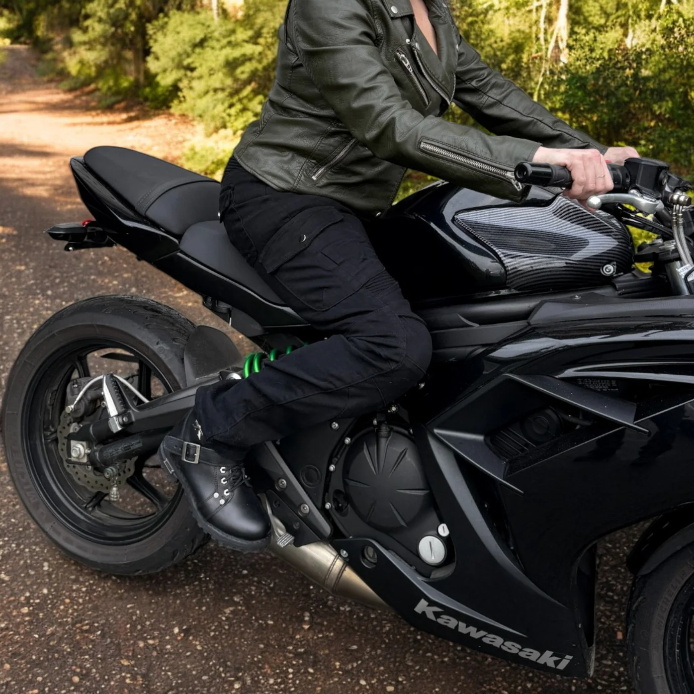 Person in leather jacket riding a black Kawasaki motorcycle.