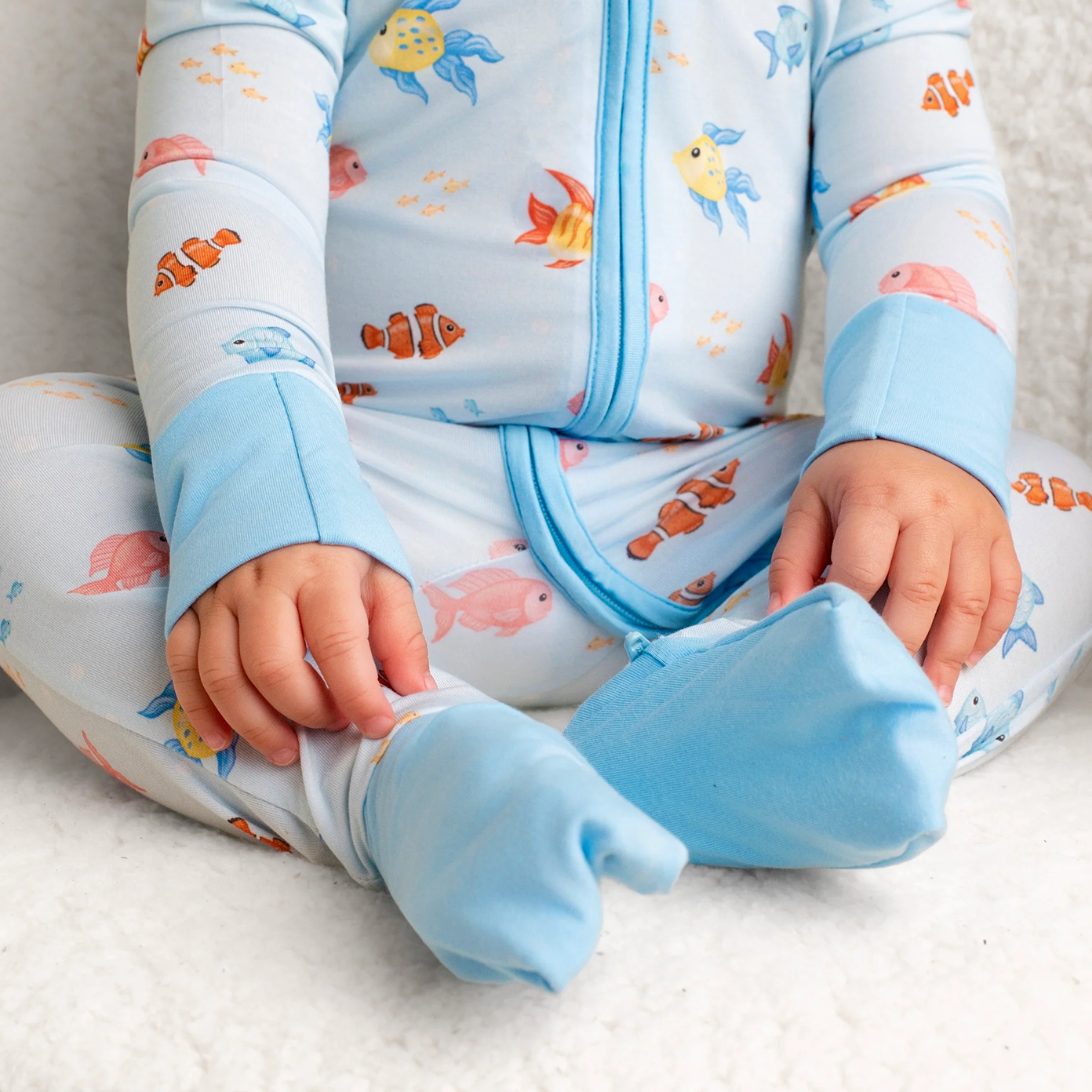 A close-up of a baby wearing light blue, footed pajamas with a colorful fish pattern.