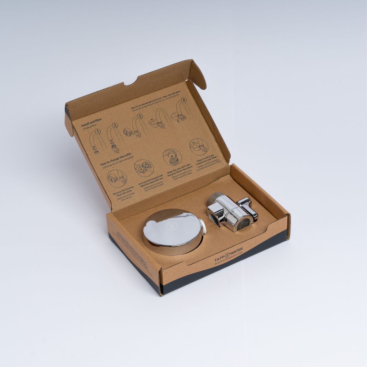 Open cardboard box with metal faucet components and installation instructions.