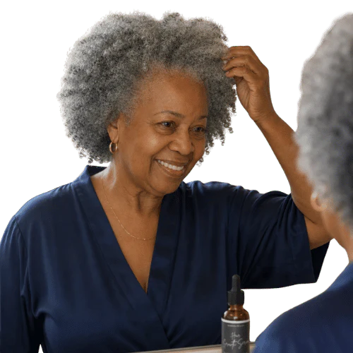 An older woman with gray, curly hair smiles at her reflection in a mirror while touching her hair.