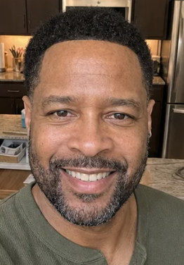 A headshot of a middle-aged Black man with a short haircut and beard, smiling at the camera.