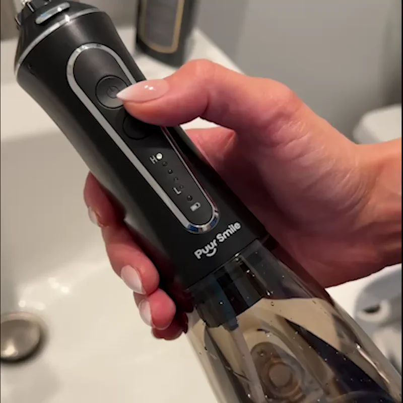 Hand holding a black Puyr Smile oral irrigator above a sink.