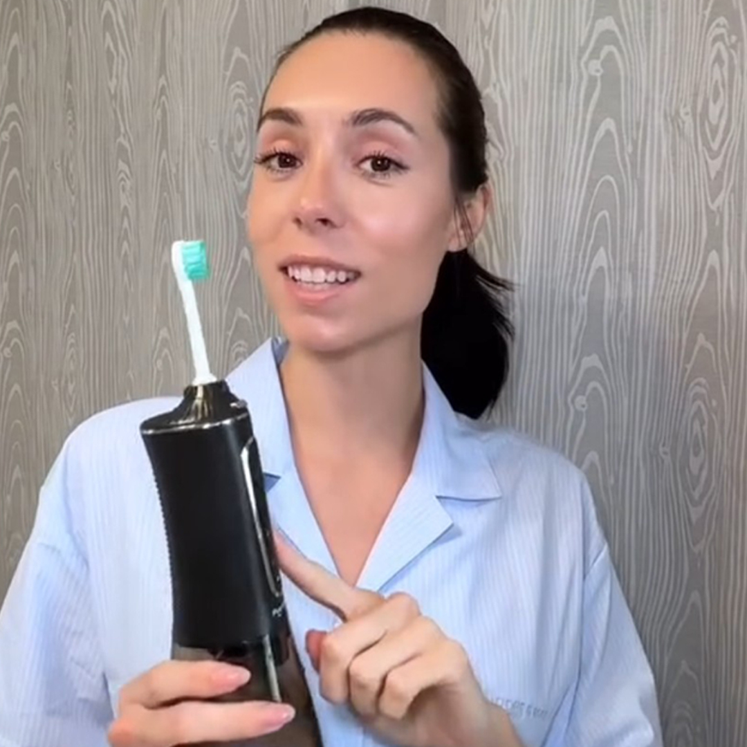 Person holding an electric toothbrush, wearing a light blue shirt.
