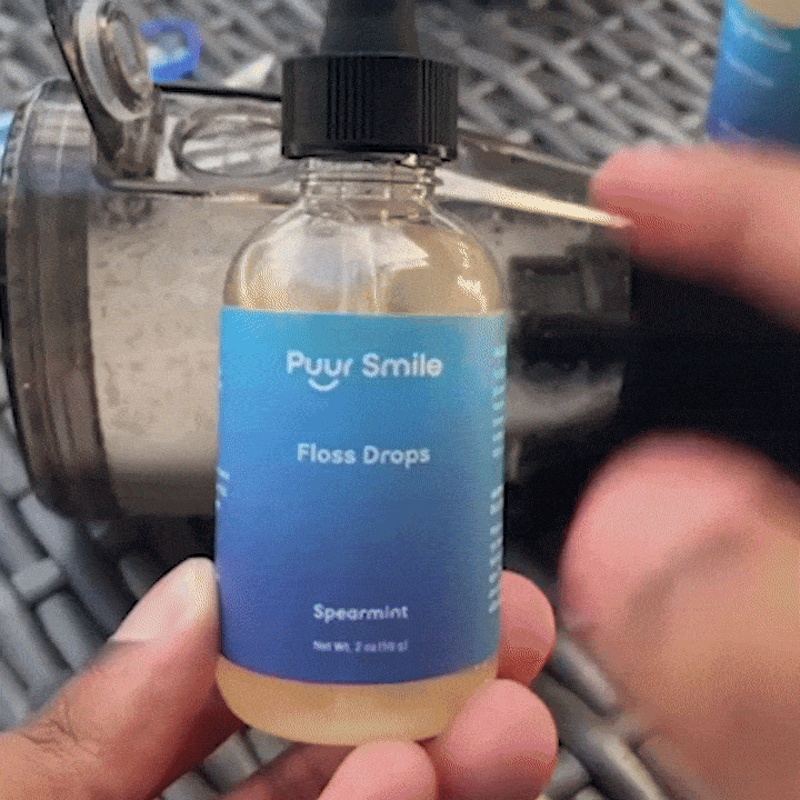 Hand holding a bottle labeled 'Puur Smile Floss Drops' with a blue gradient label.
