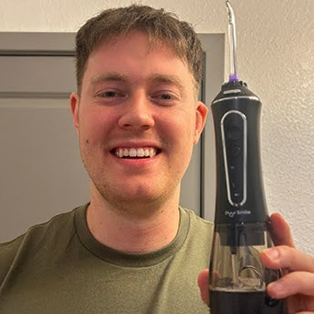 Person holding a black electric toothbrush against a light-colored wall.