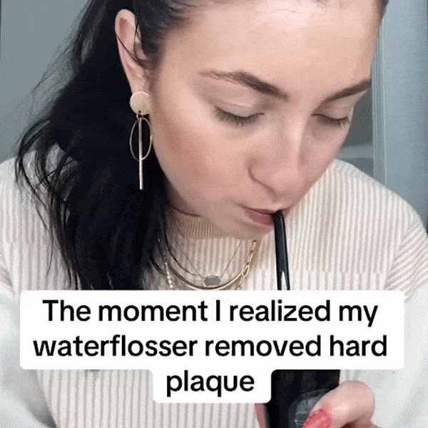 Person using a water flosser while reading a caption about removing plaque.