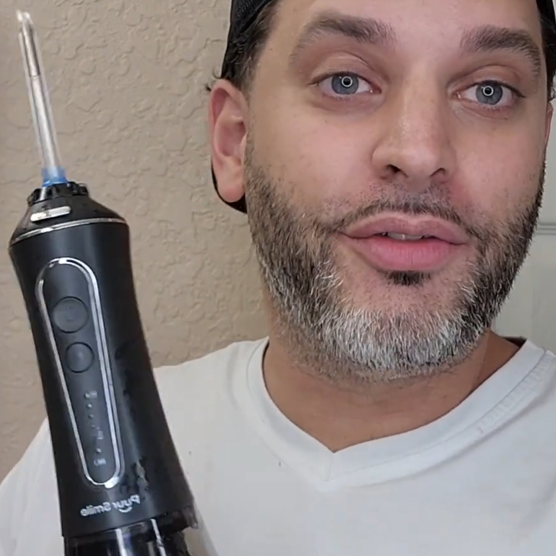 Person holding a black electric water flosser, wearing a white shirt.