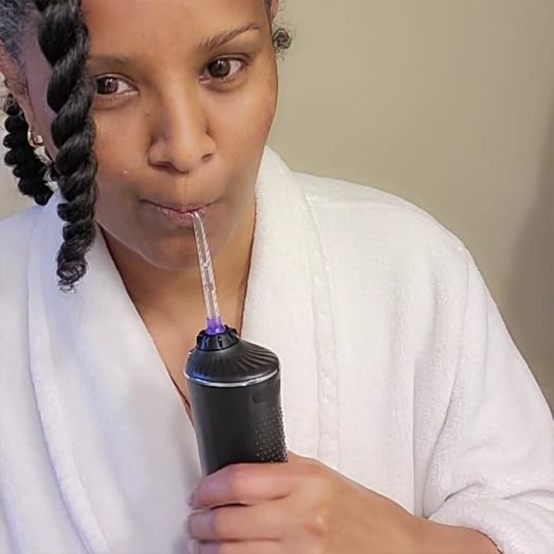 Person using a handheld water flosser in a white robe.
