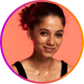 A circular headshot of a smiling woman with her curly dark hair pulled back against a colorful background.