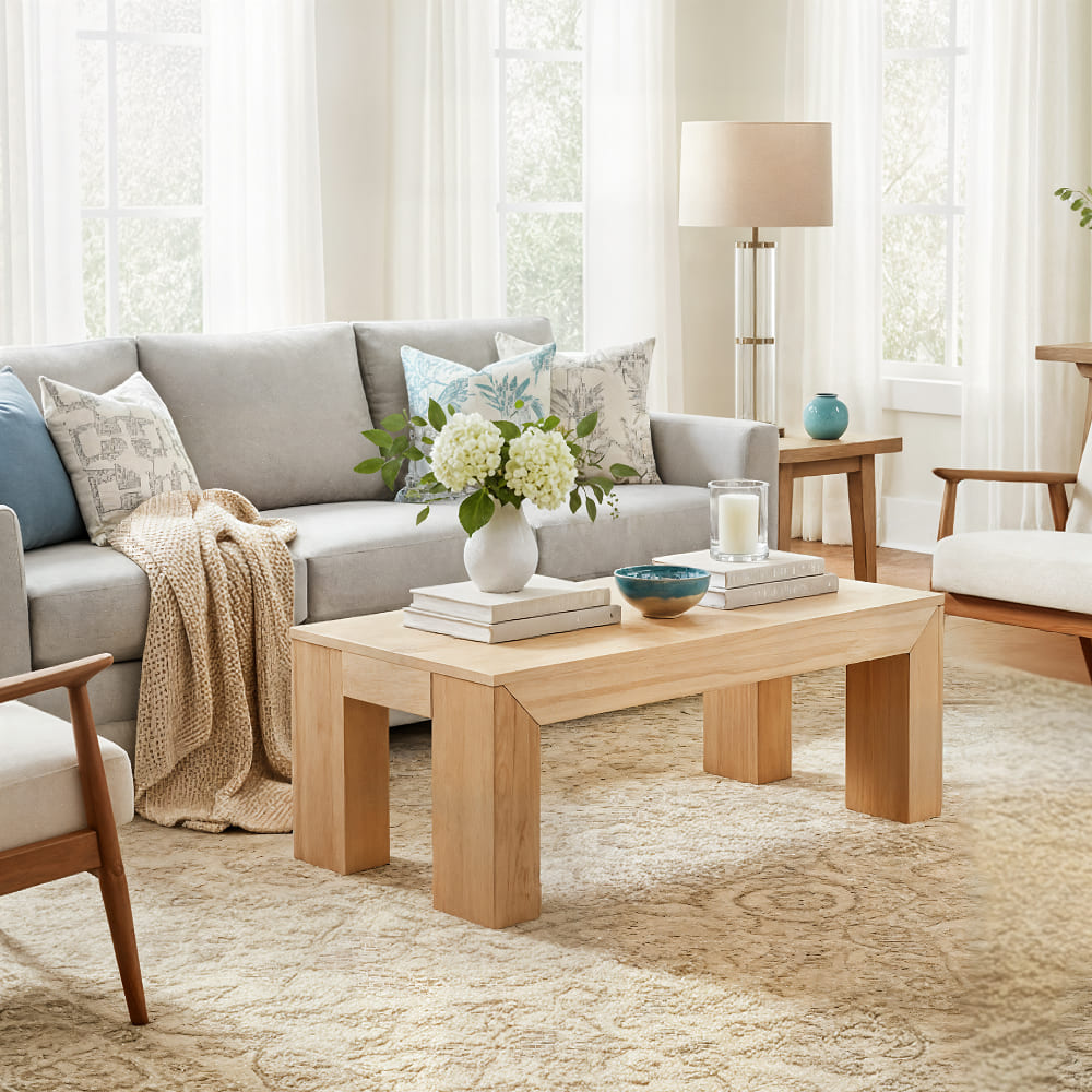 Blonde coffee table in naturally light room with grey couch.