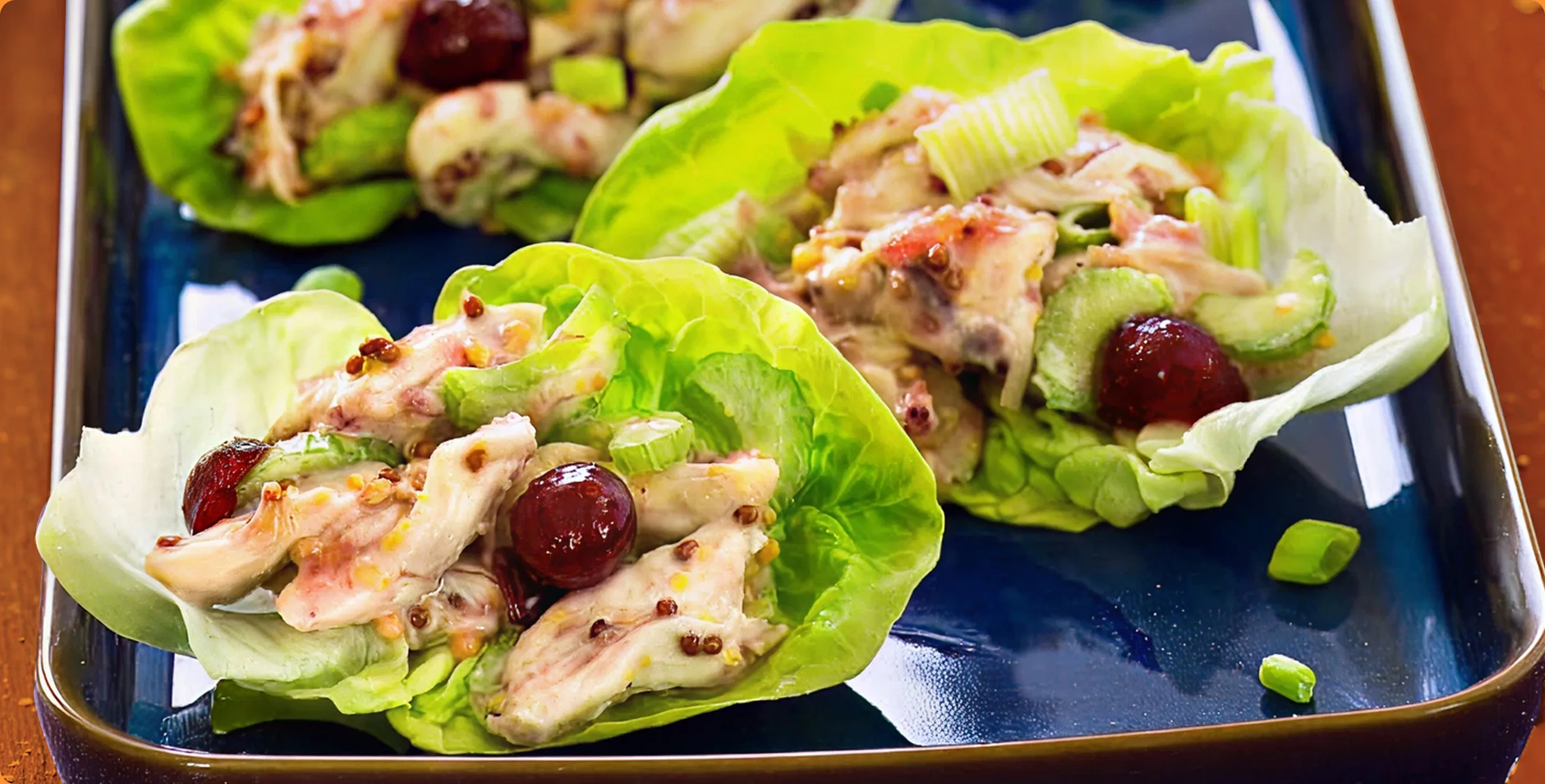 Lettuce wraps with chicken, grapes, and celery on a blue plate.