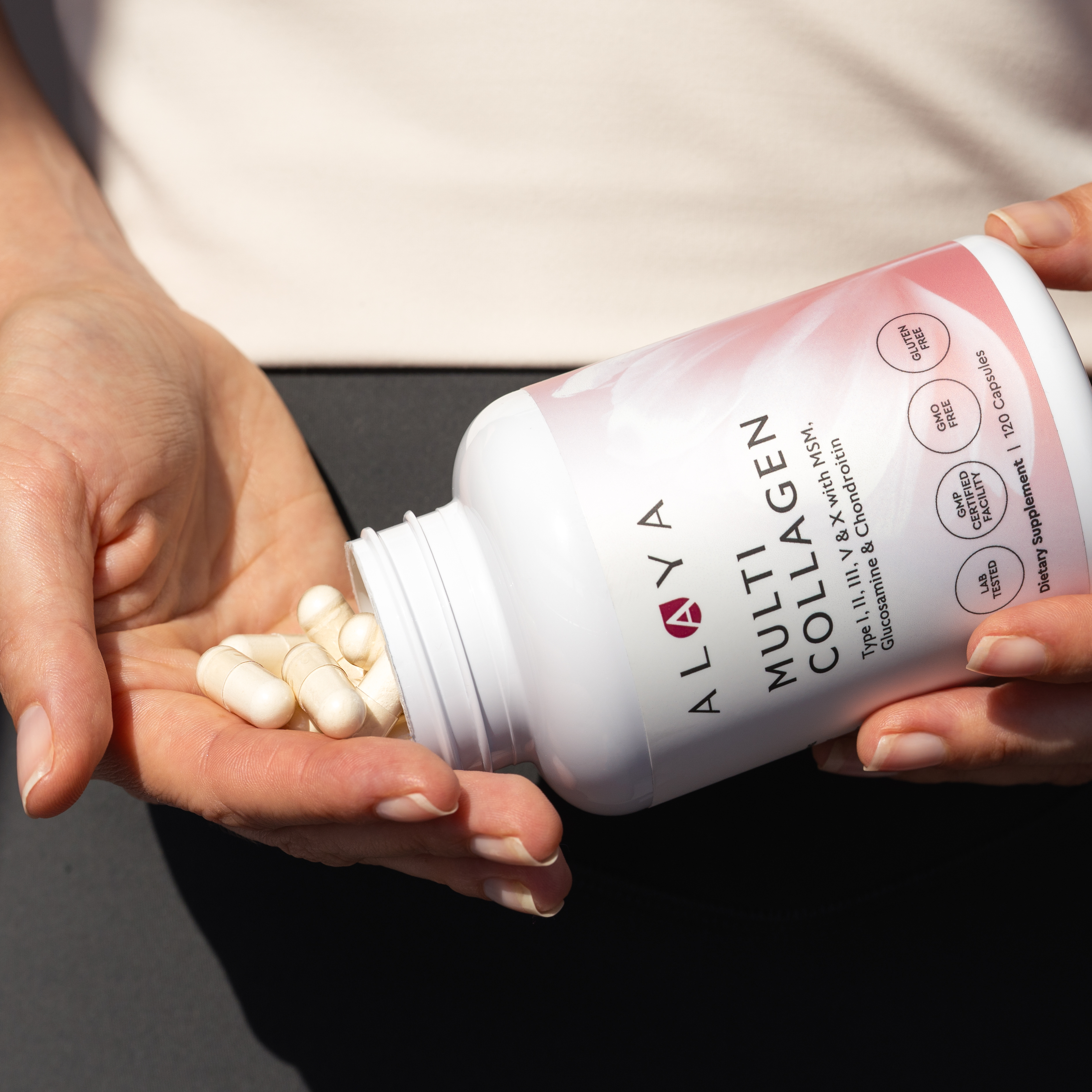 A person pours Alaya Multi Collagen capsules from a white bottle into their cupped hand.