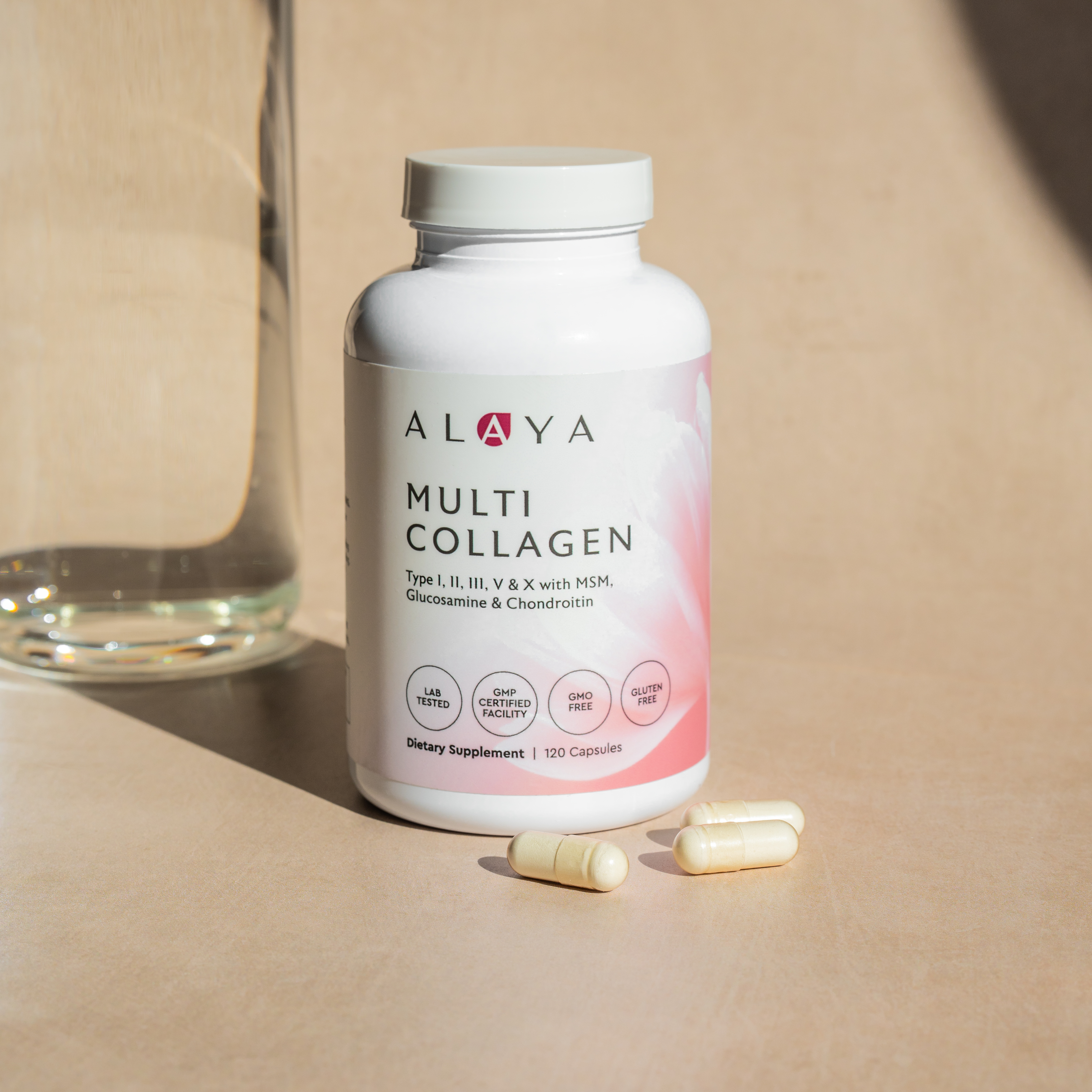 A bottle of Alaya Multi Collagen supplements with three capsules and a glass of water on a surface.