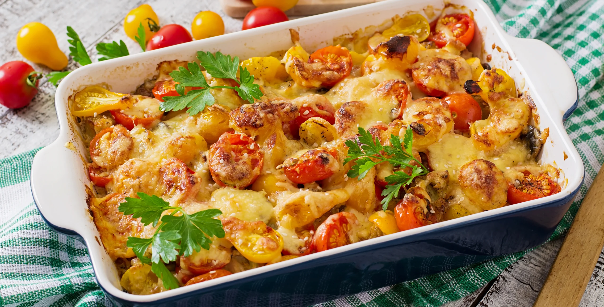 Baked dish with cherry tomatoes, cheese, and parsley in a white casserole dish.