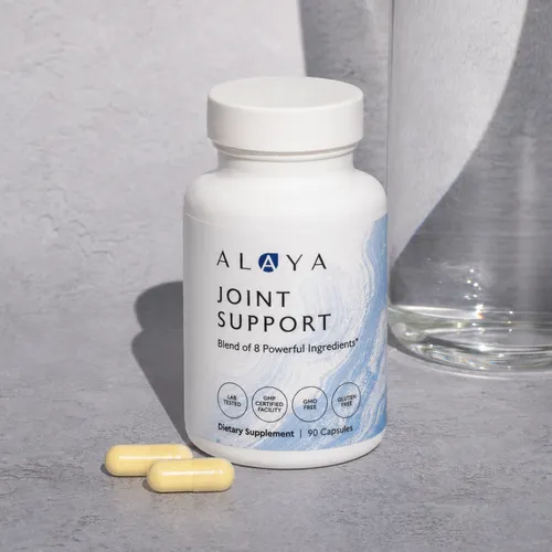 A white bottle of Alaya Joint Support dietary supplement, with two capsules lying next to it.