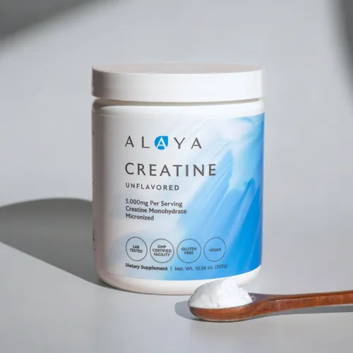 A white container of Alaya Creatine powder with a wooden spoon holding a scoop of the powder.