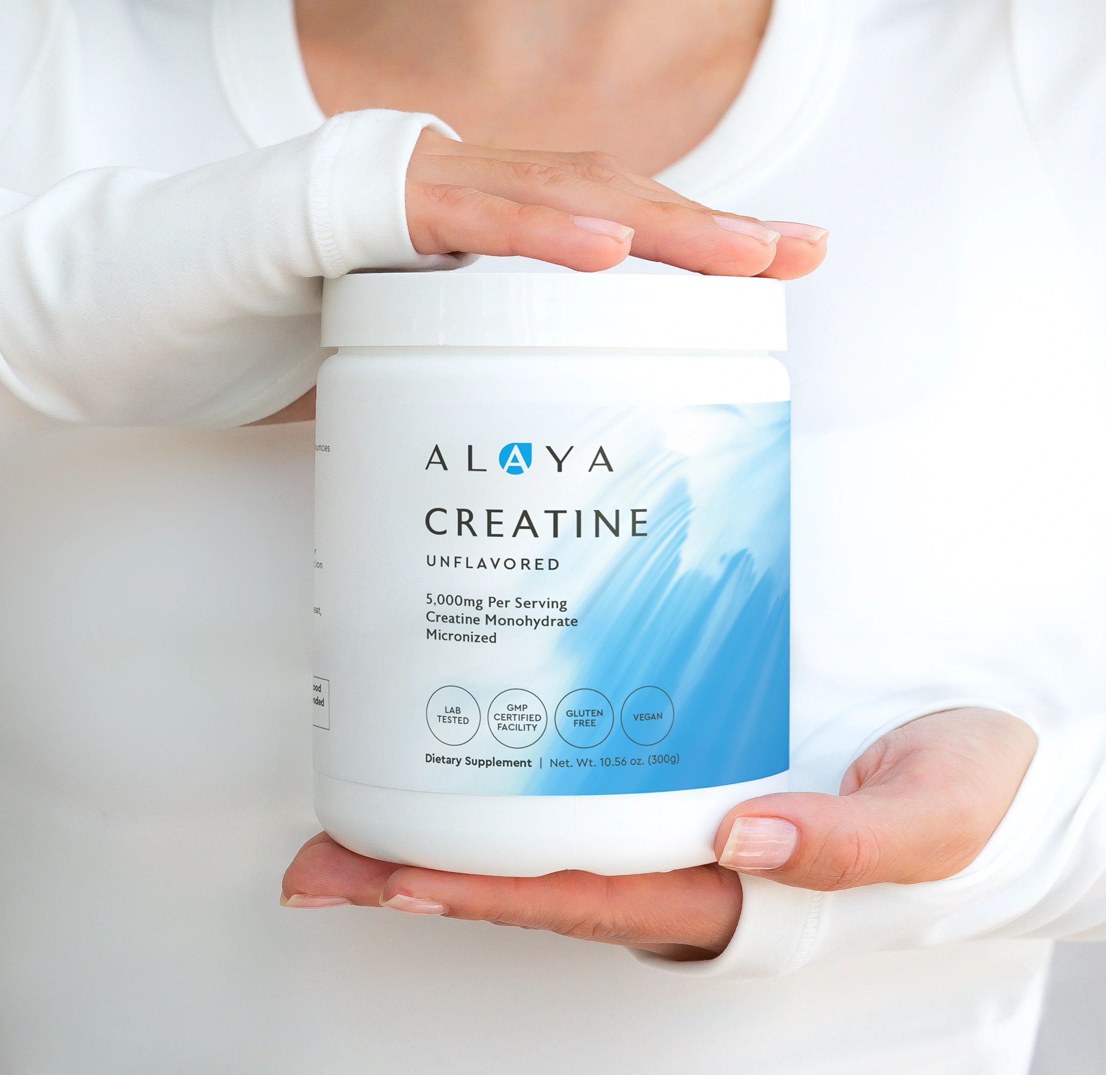 A person in a white shirt holds a jar of Alaya Unflavored Creatine dietary supplement.