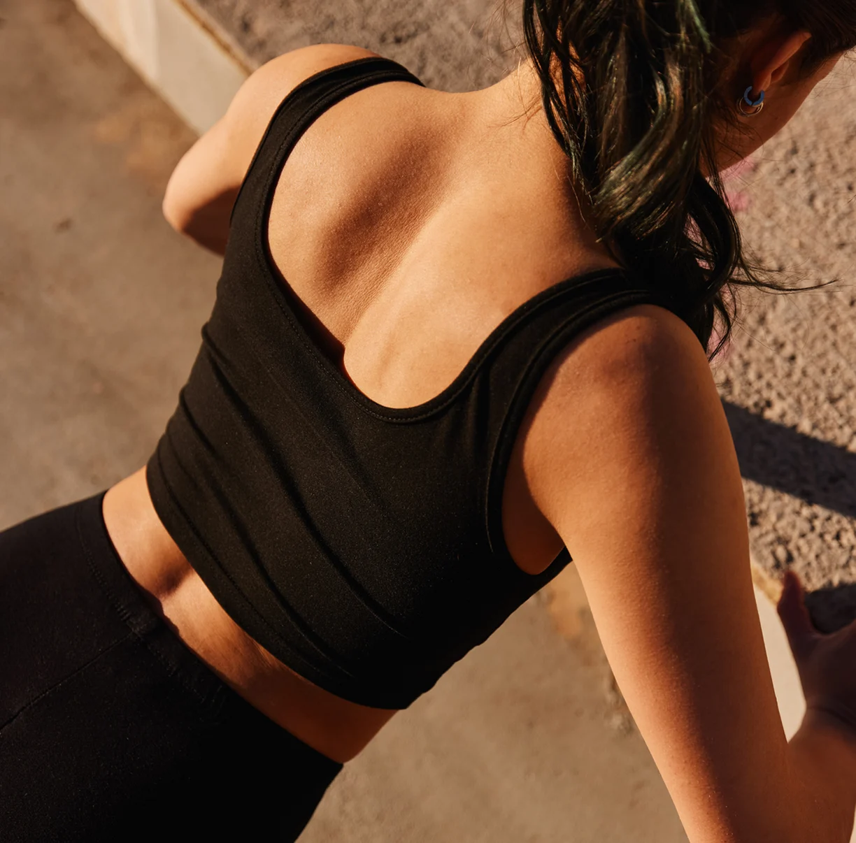 A high-angle view of a person's back in a black tank top, leaning forward against a wall.