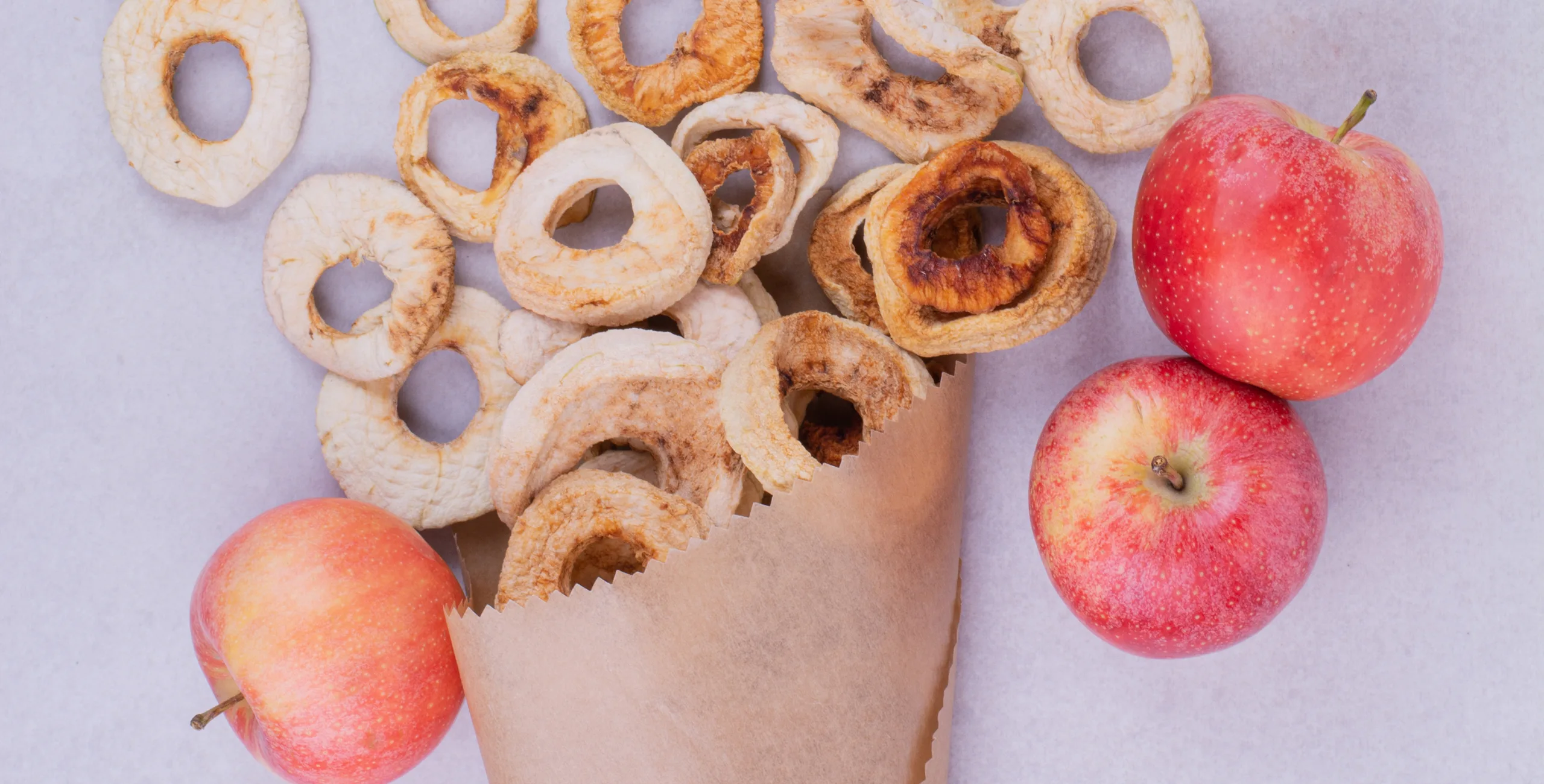 Dried apple rings in a paper cone with fresh red apples.