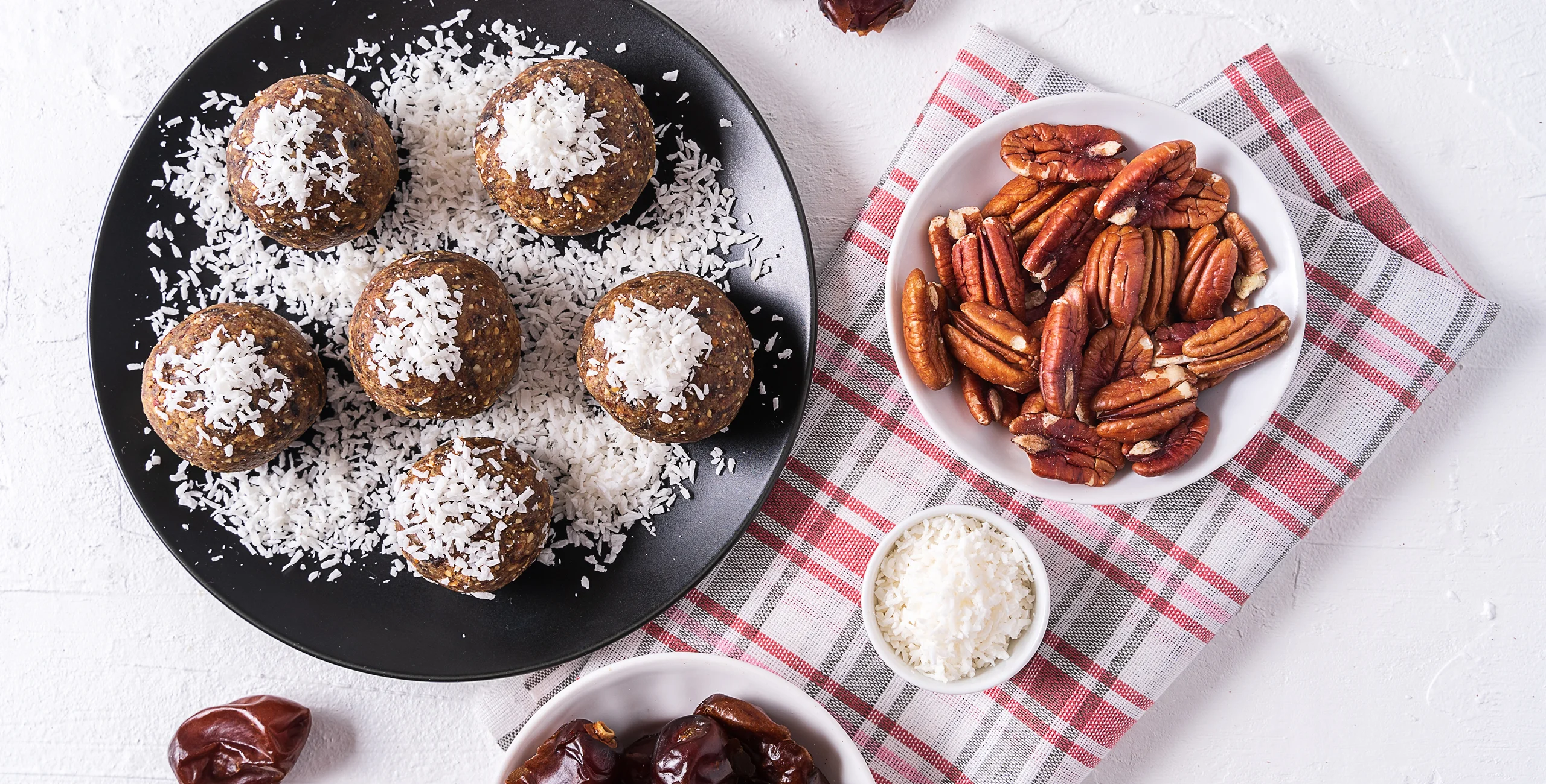 Energy balls with coconut, pecans, and dates on a plaid cloth.