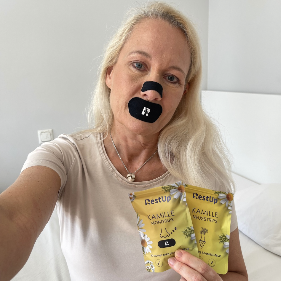 A woman with a nose strip and mouth tape holds up two pouches of RestUp Kamille strips.