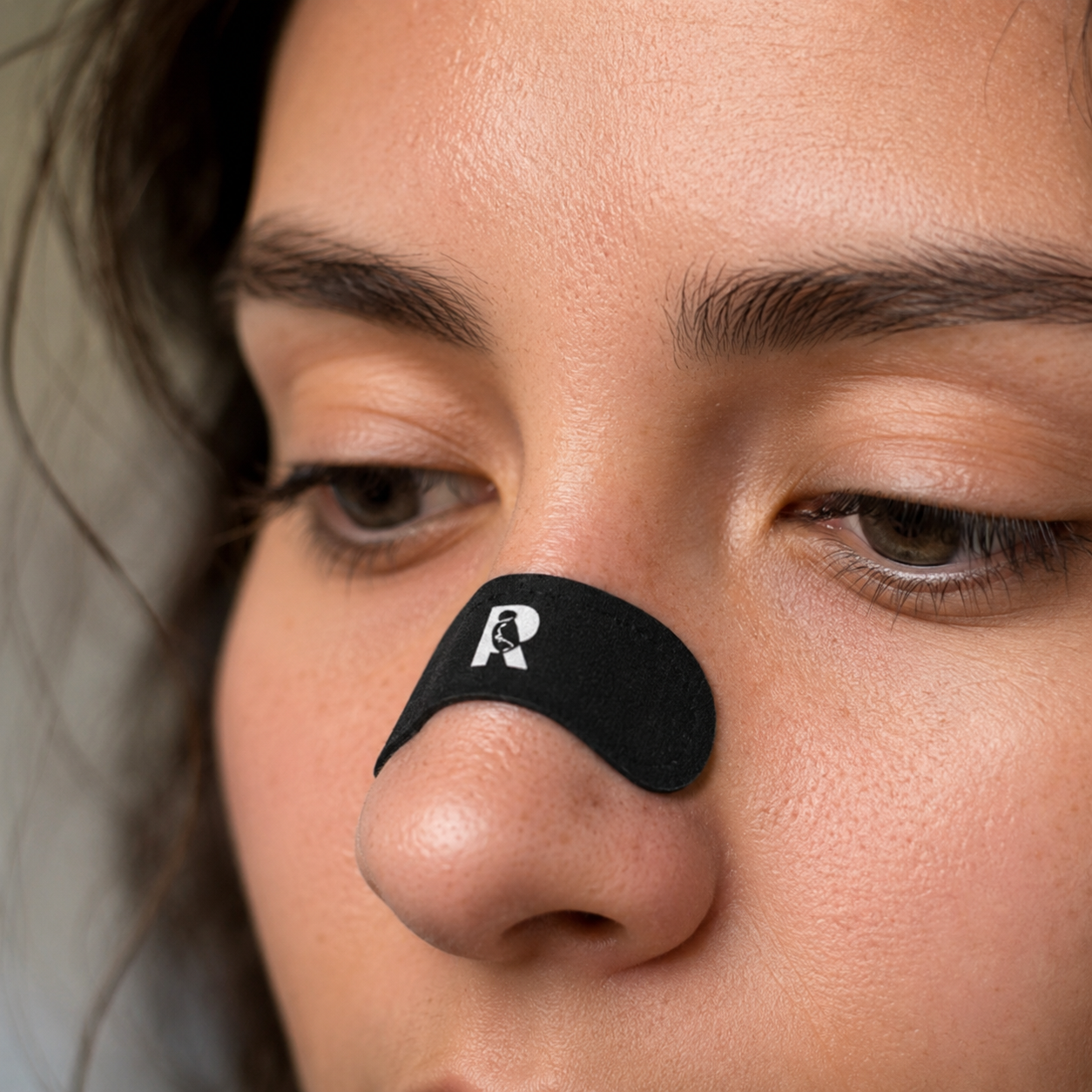 A close-up of a person's face with a black nasal strip across the bridge of their nose.