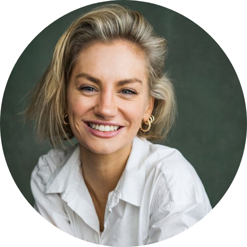 Smiling person with short blonde hair wearing a white shirt, against a dark background.