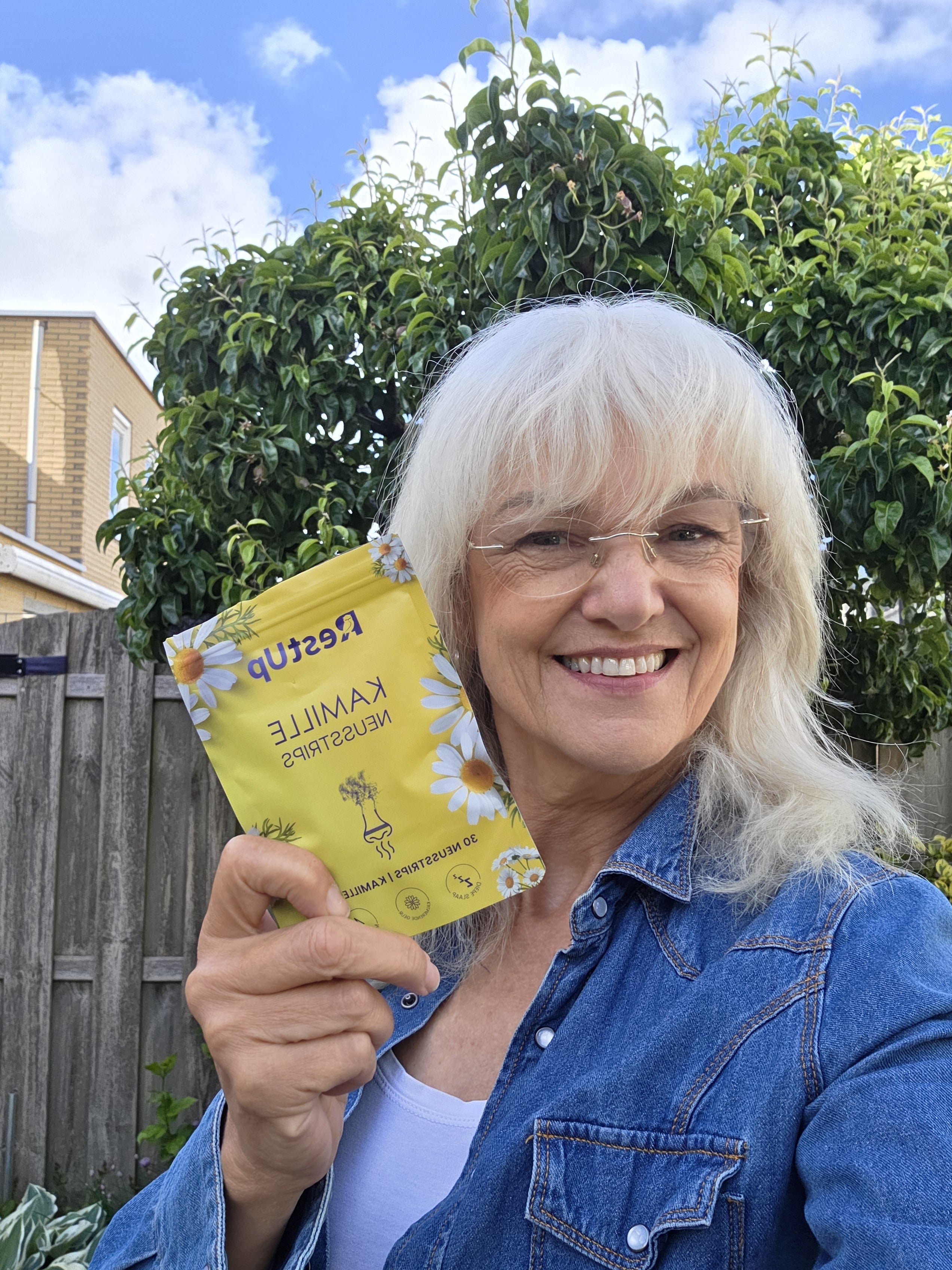 Person smiling, holding a yellow packet with flowers, standing in a garden.