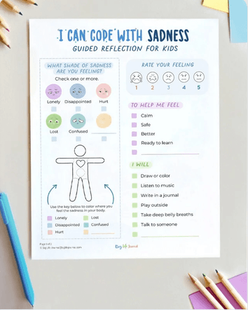 A worksheet for kids titled 'I Can Cope With Sadness' shown on a desk with colored pencils.