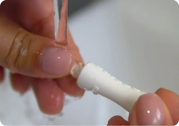 Hands rinsing a brush head under running water.