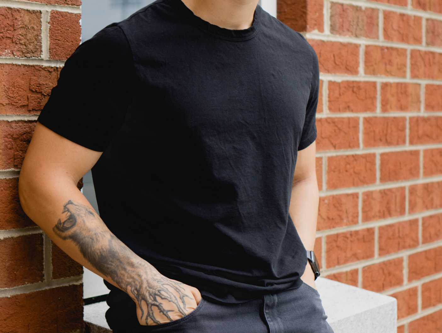 A man in a grey t-shirt, khaki pants, and sunglasses walks on a sidewalk next to trees.