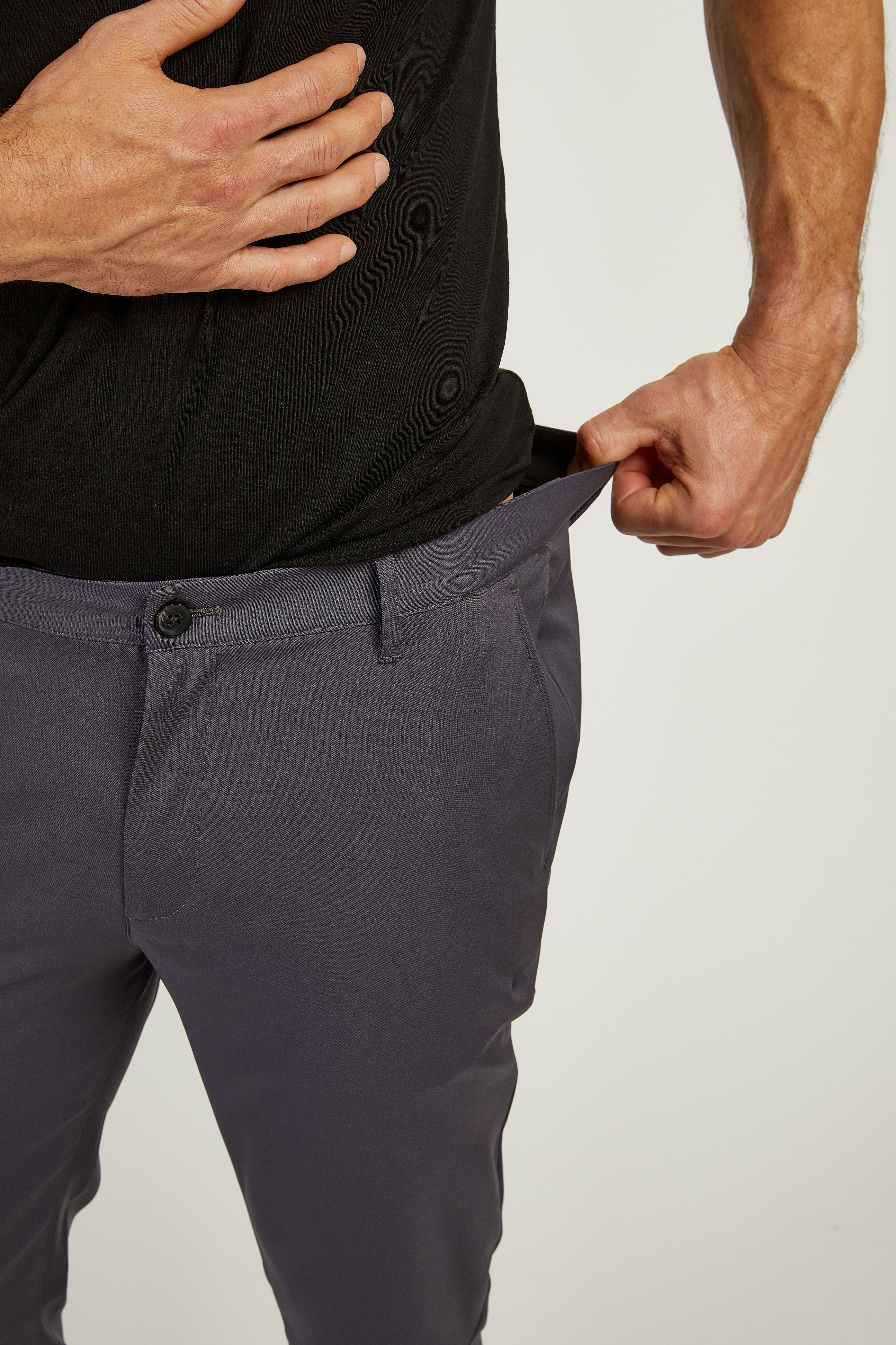 Person wearing black shirt and gray pants, pulling waistband to show looseness.