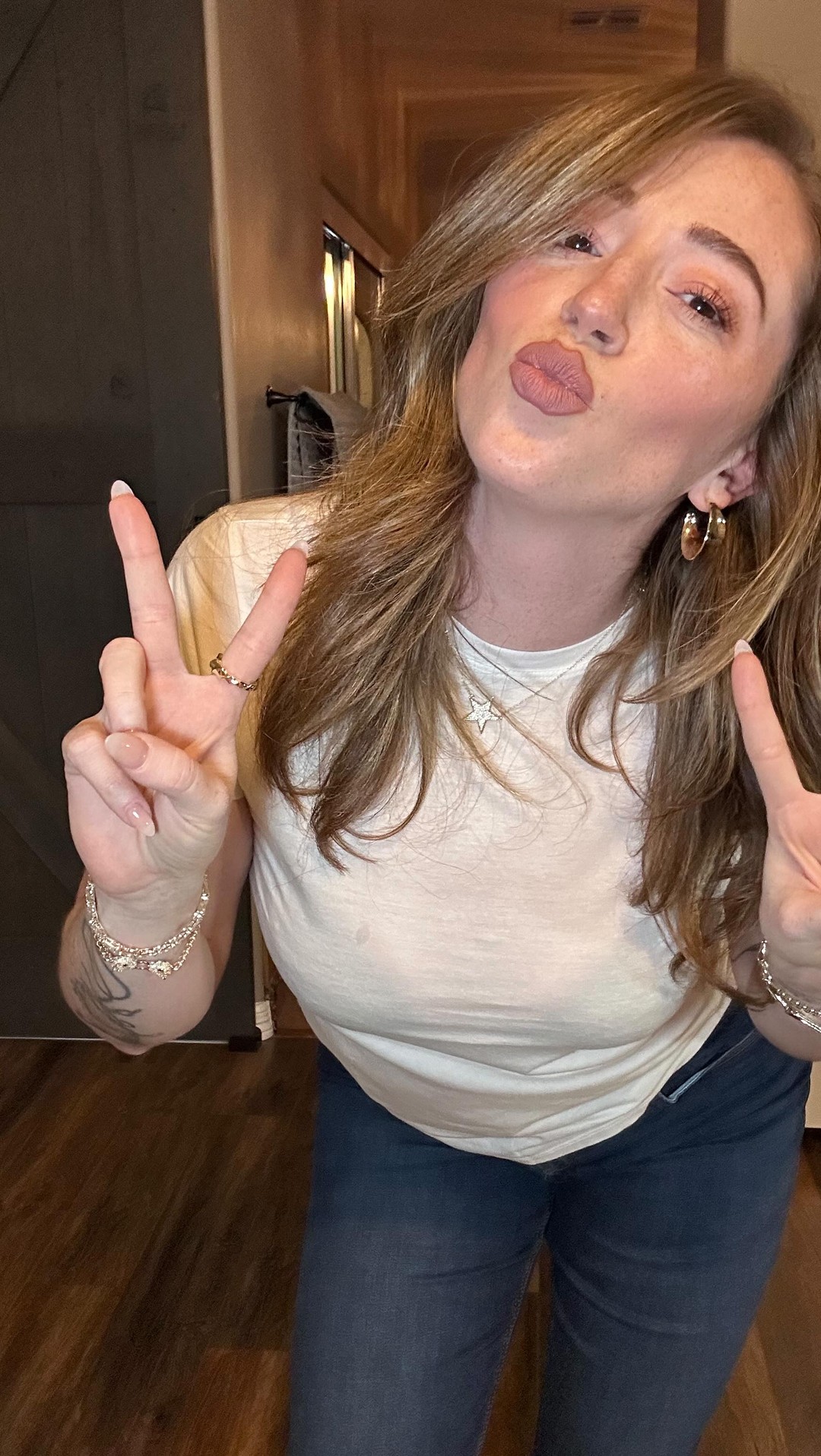 Person in white shirt making peace signs with both hands indoors.