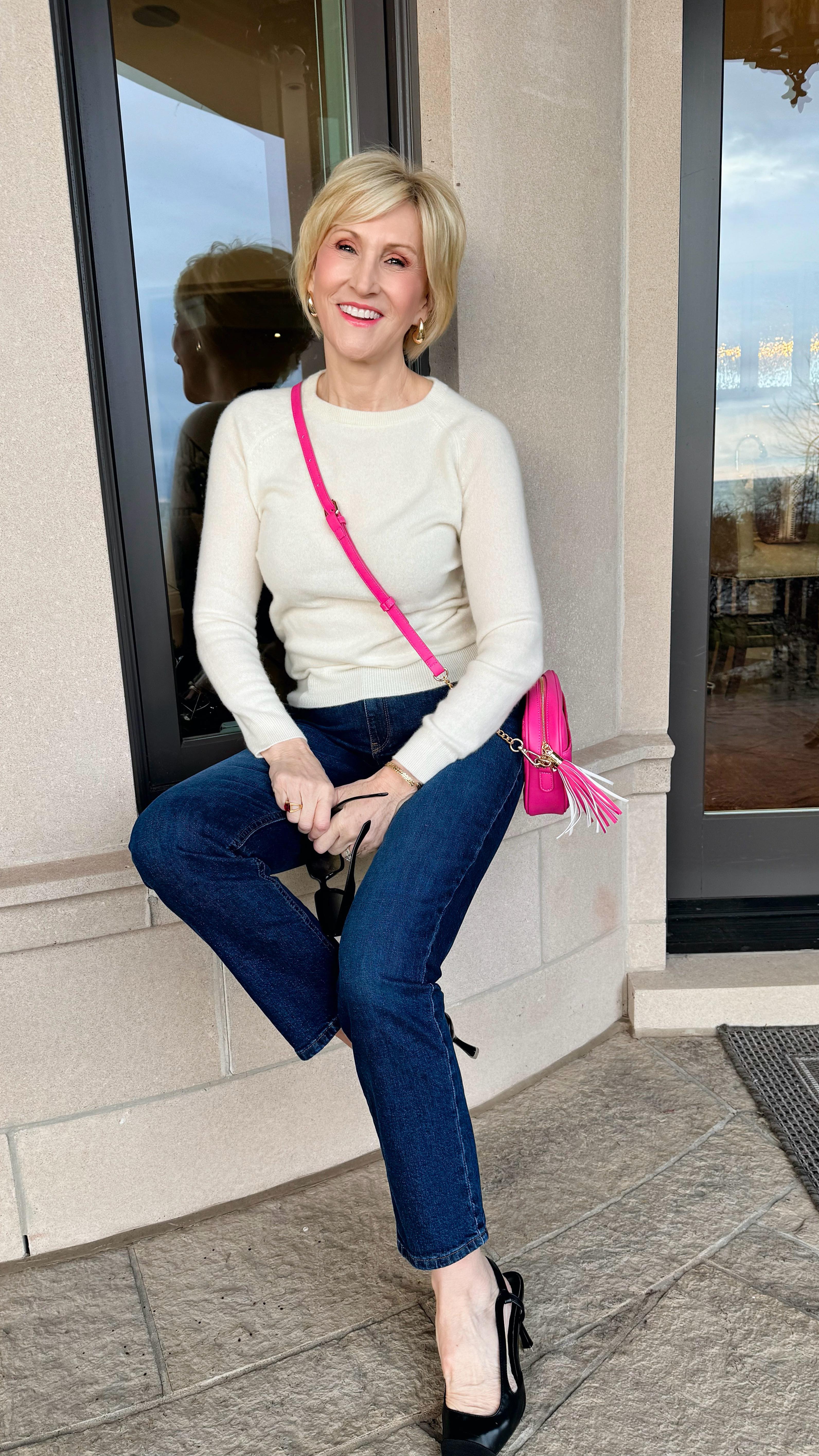 Person sitting on a ledge, wearing a white sweater and jeans, with a pink bag.