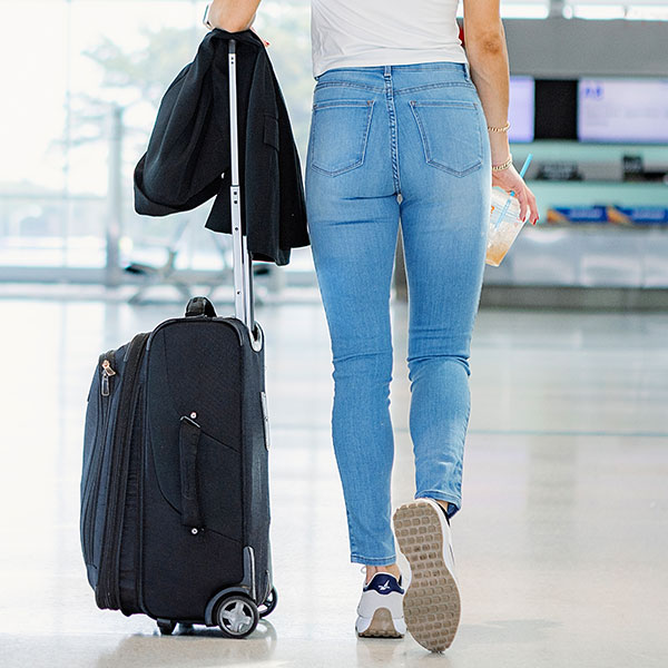 Person walking in an airport with a suitcase and drink.