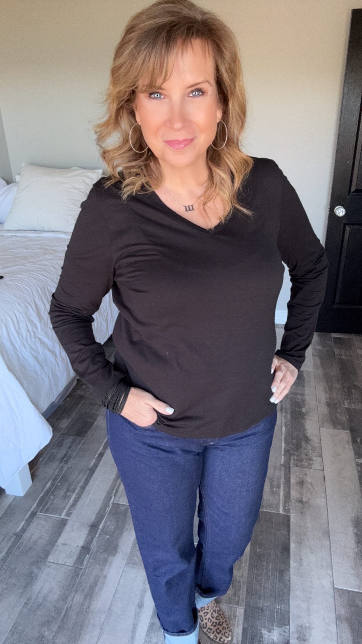 Person in a black shirt and jeans standing in a room with a bed.