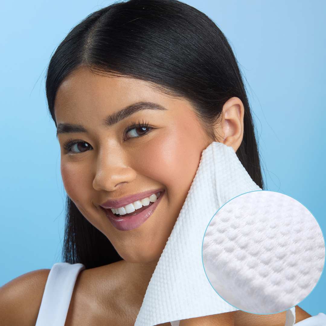 Smiling person using a textured white cloth on their face against a blue background.