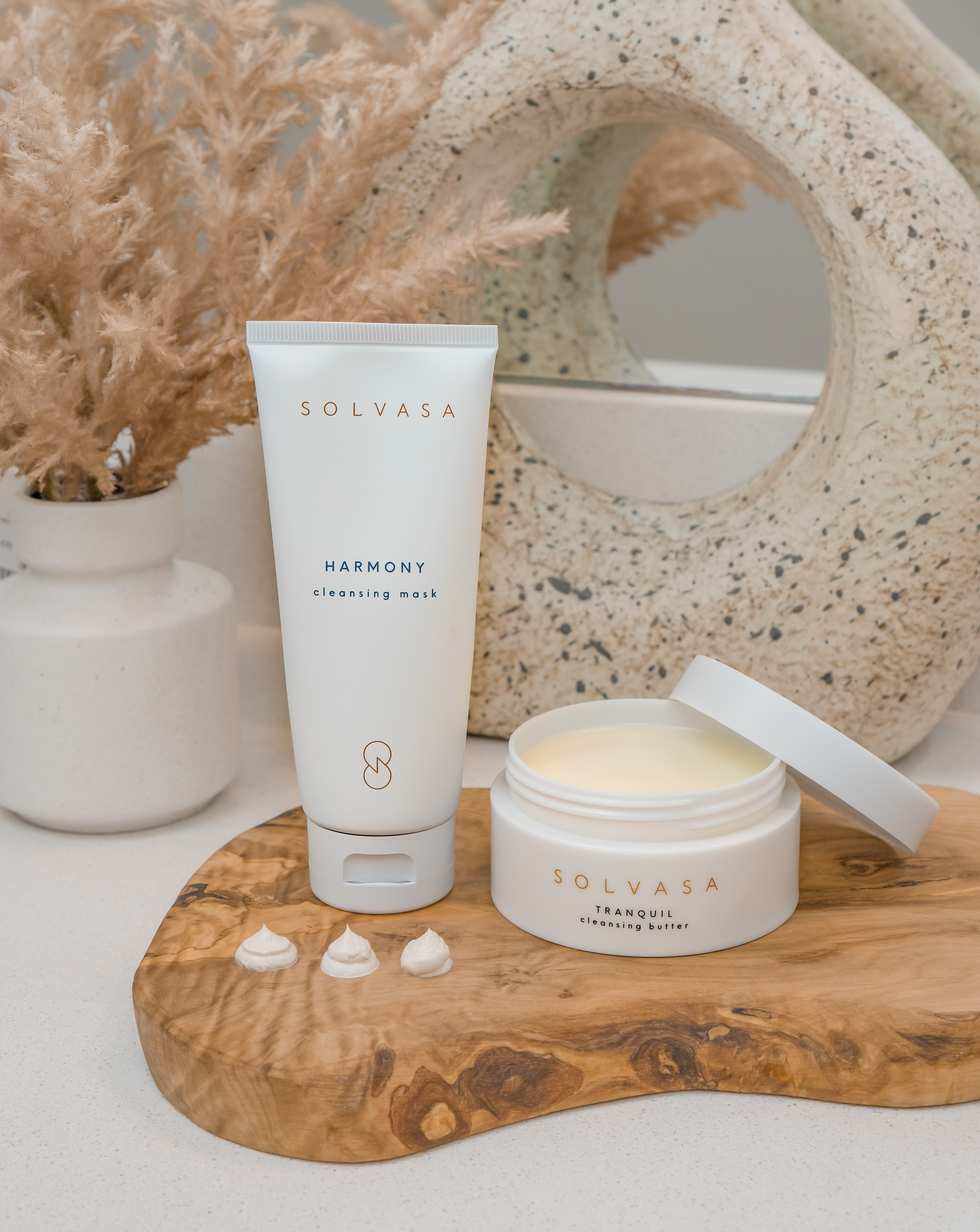 A wooden spoon scoops white cleansing butter from a jar sitting in a bed of yellow powder.