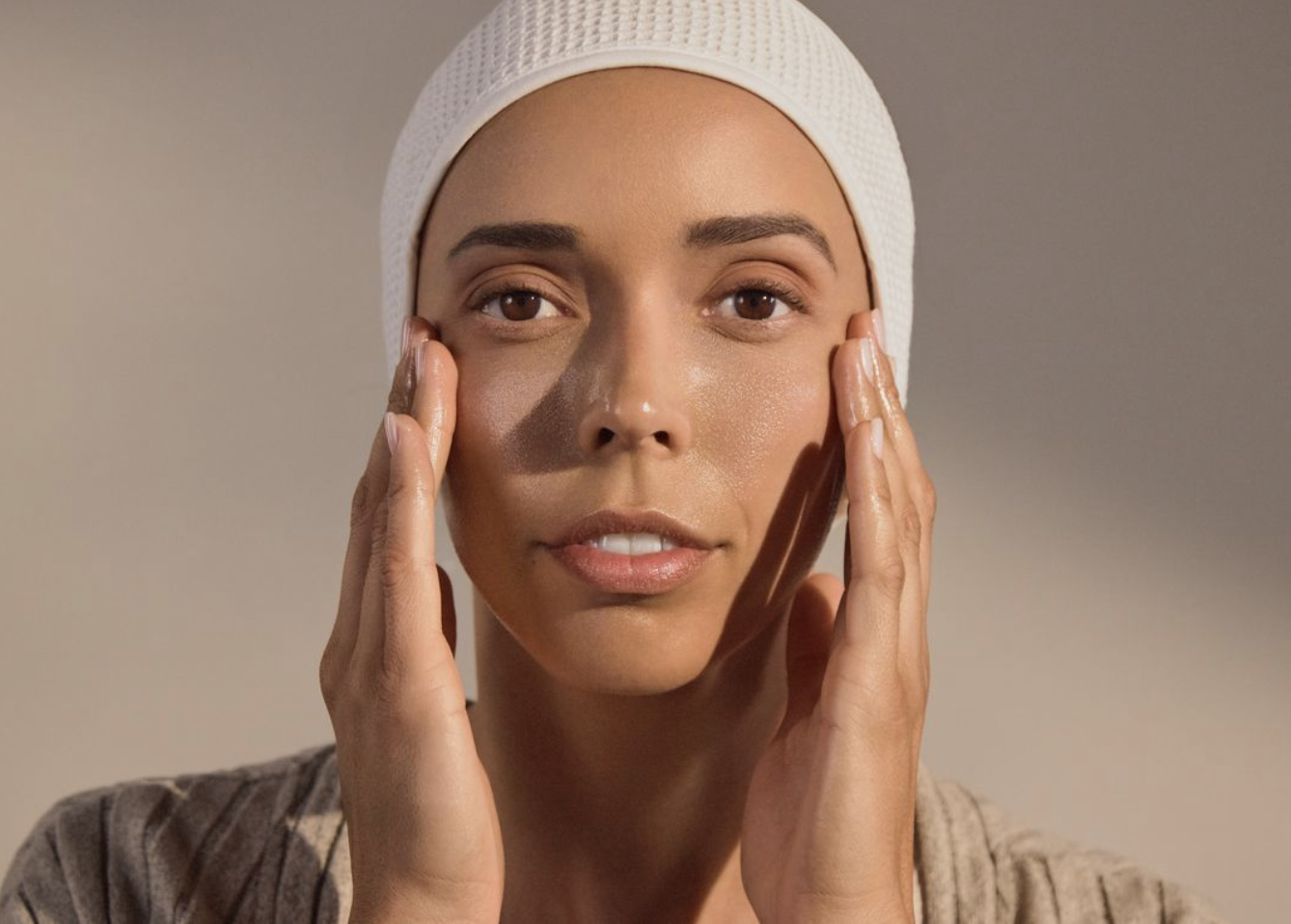 A woman wearing a white head covering gently touches both sides of her face with her hands.