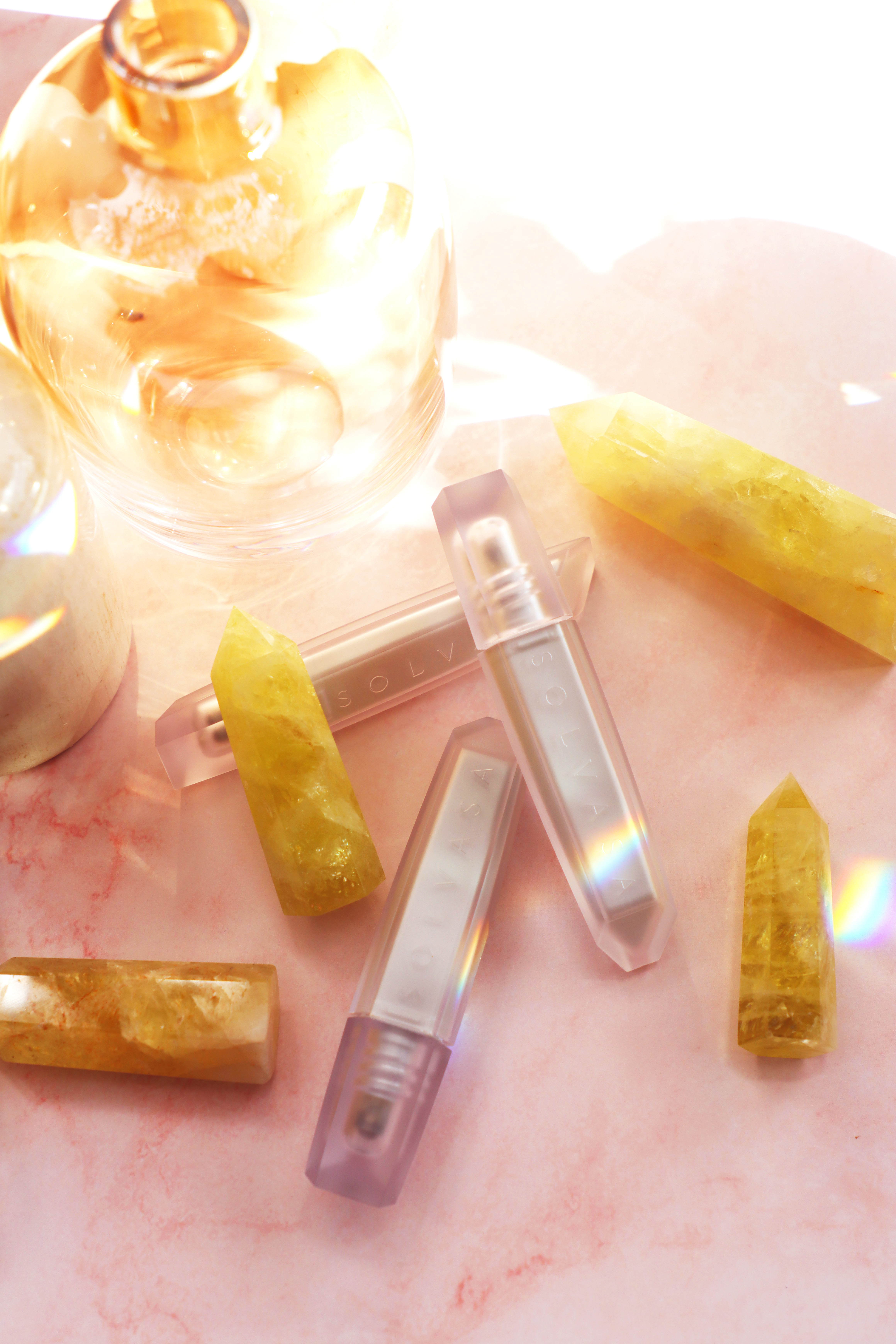 An overhead shot of translucent cosmetic bottles and yellow crystals on a pink marbled surface.