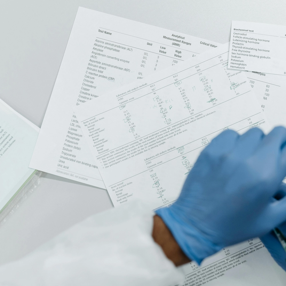 A person wearing a blue medical glove examines a laboratory test results report.