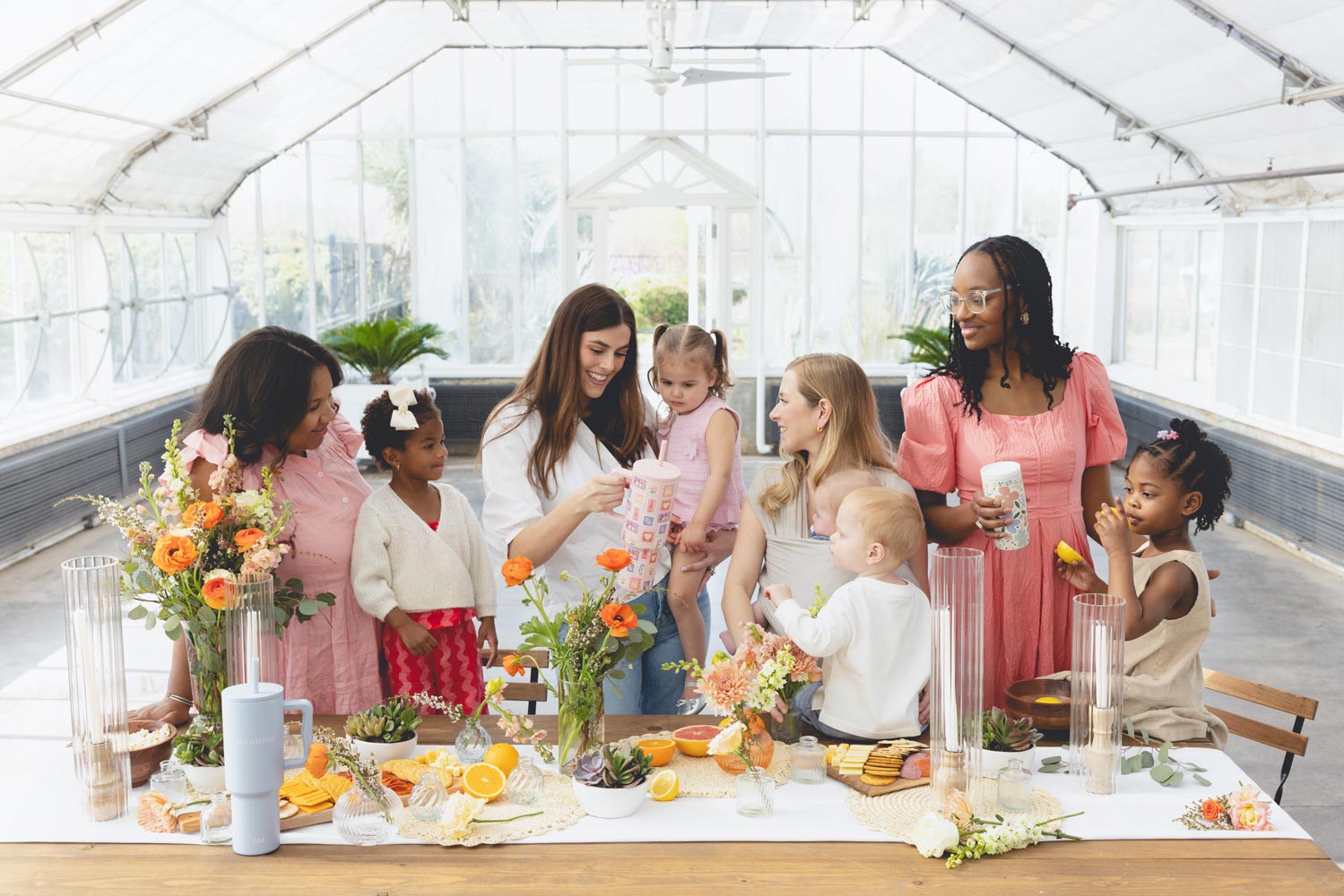 Group of women and children gathered around a table with flowers and snacks.