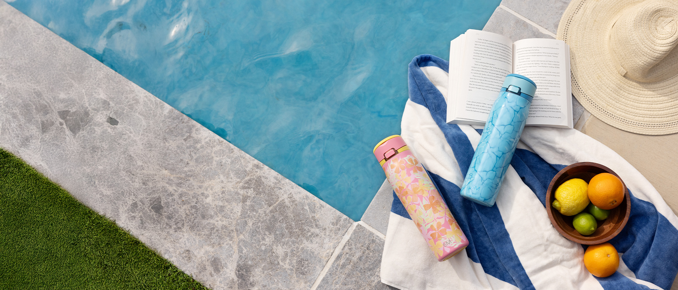 Two colorful water bottles arranged with a hat, fruit, and flip-flops by a pool.