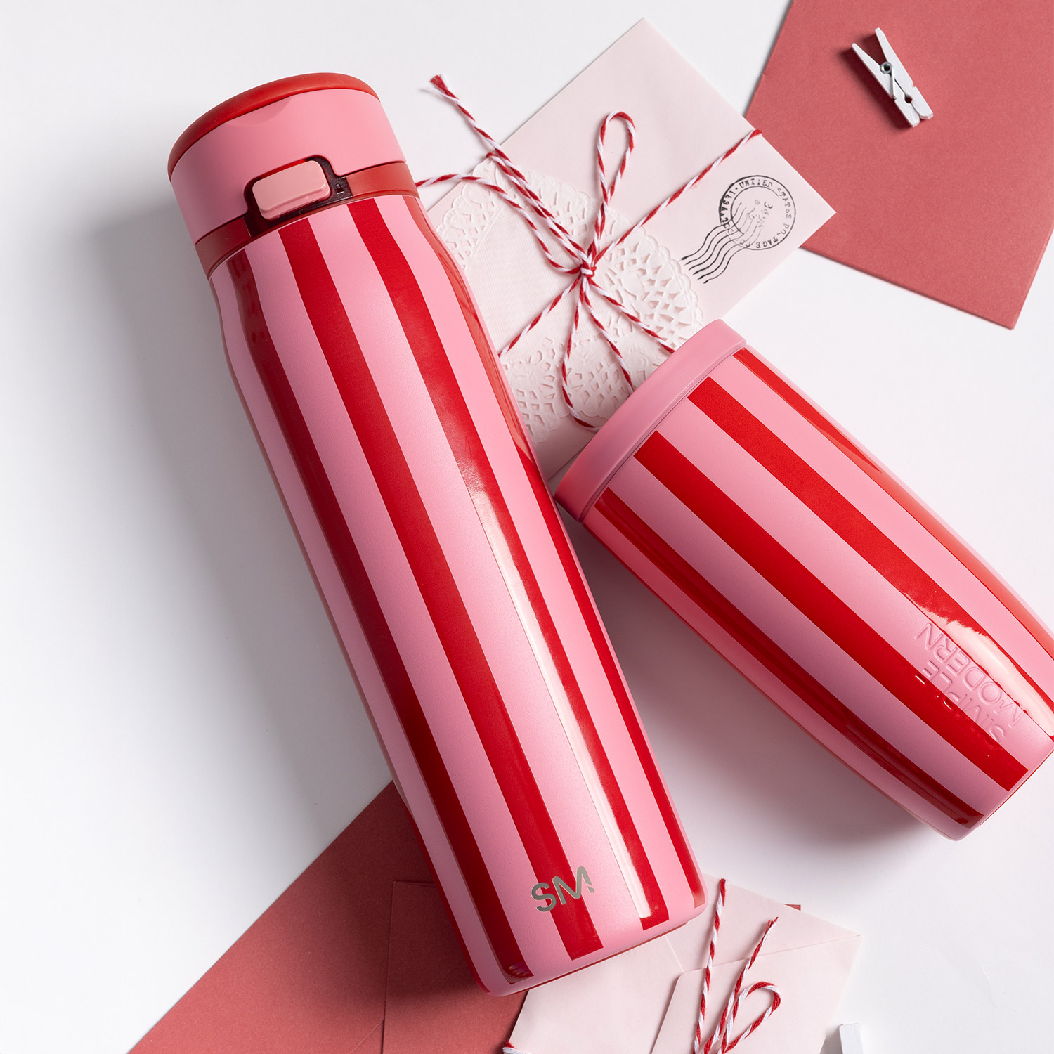 A pink and red striped water bottle and tumbler arranged with envelopes and string on a white surface.
