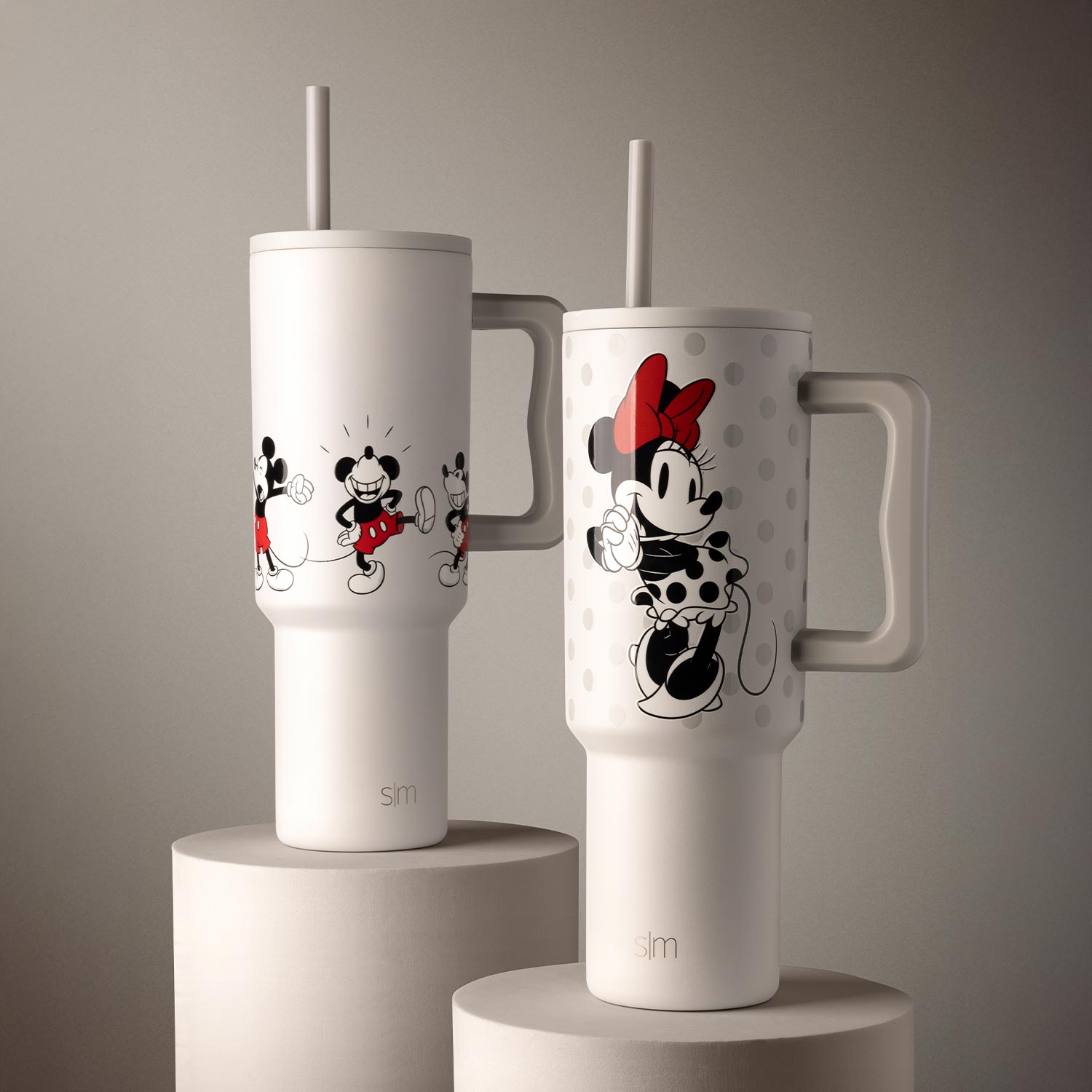 Two white tumblers with cartoon characters and straws on cylindrical stands.
