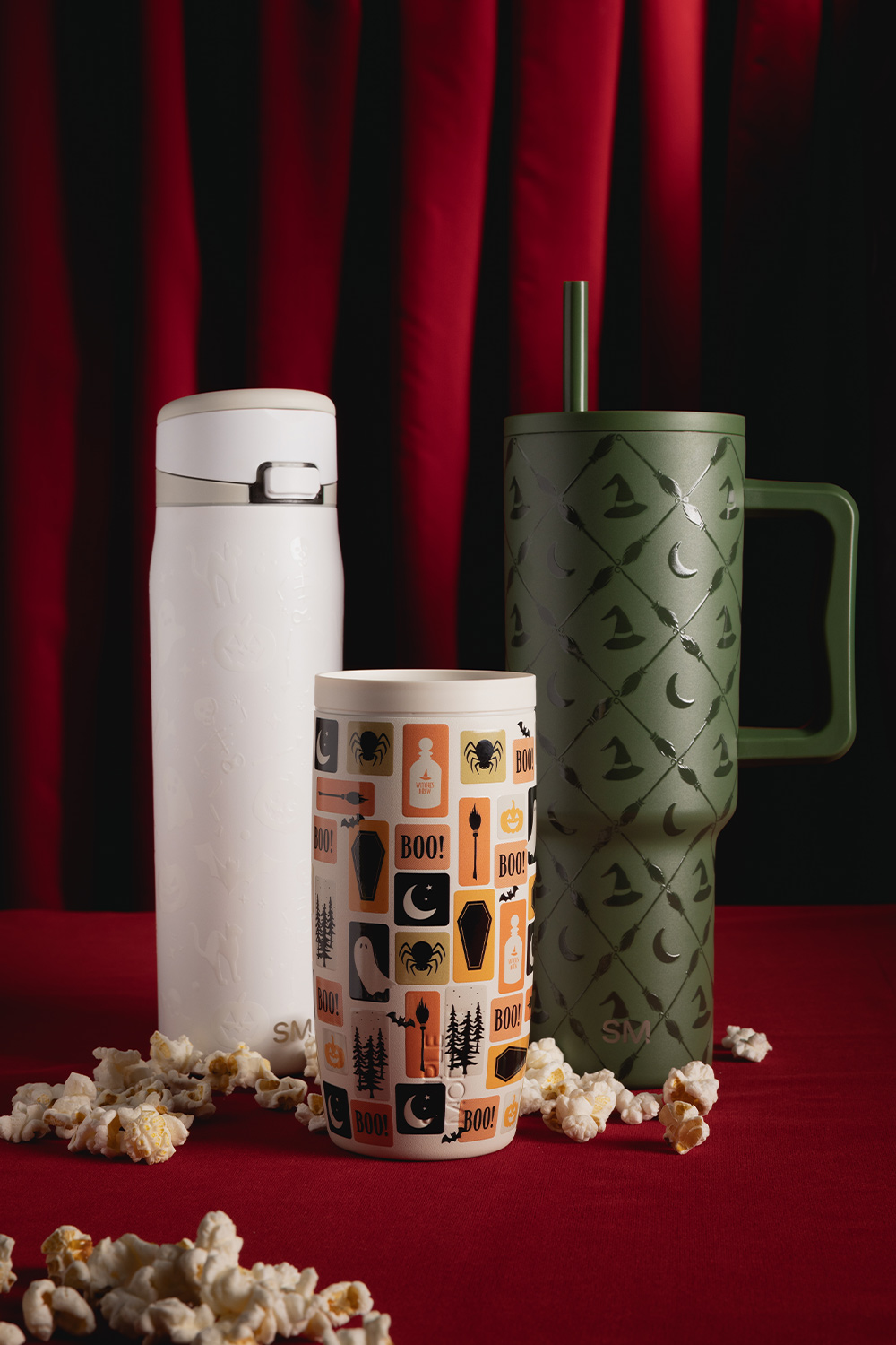 Three decorated tumblers on a red table with scattered popcorn.