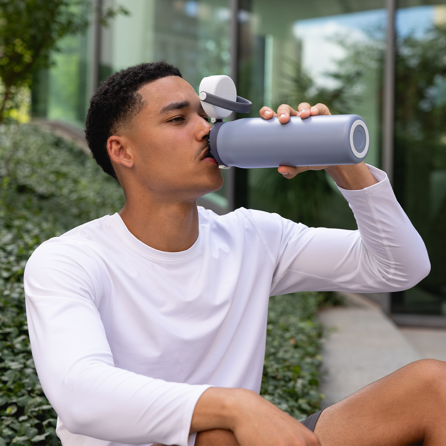 Man in white shirt drinking from a grey water bottle outdoors.