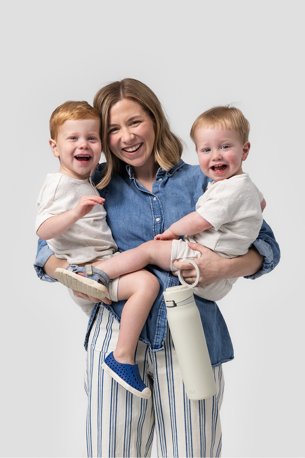 A person holds a floral tumbler while pushing a stroller handle outdoors.