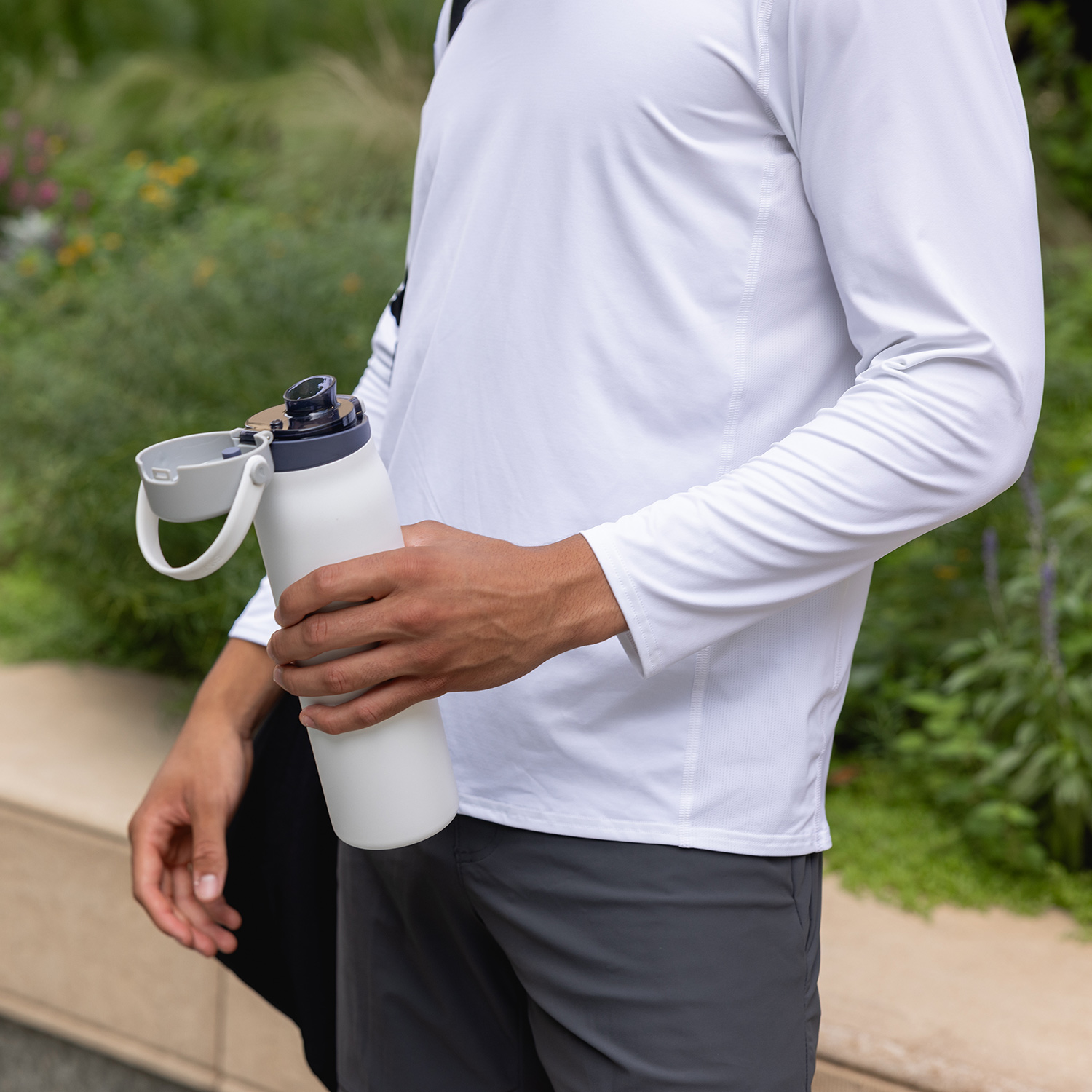 Person in white shirt holding a white water bottle outdoors.