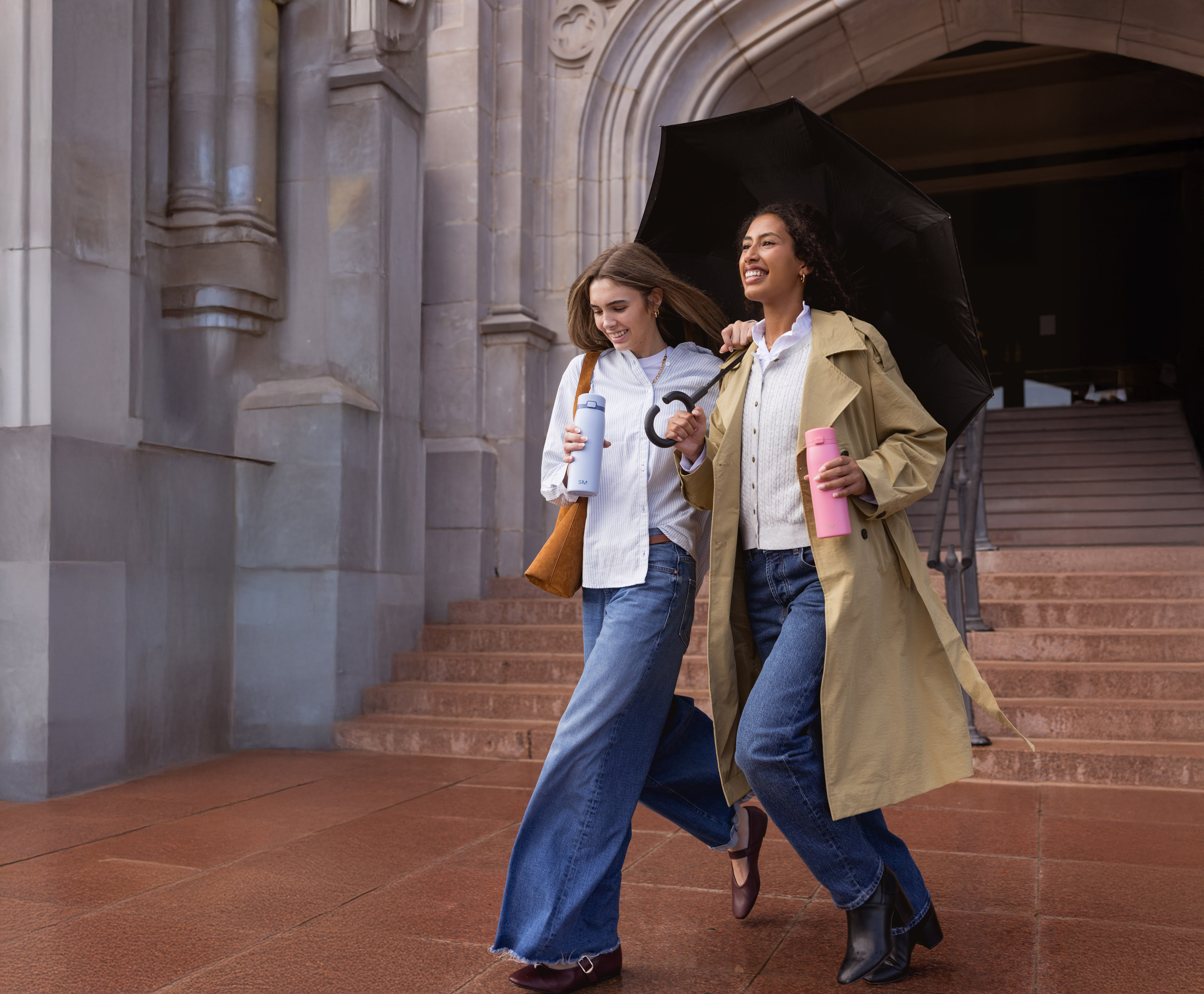 Two women walking outside with an umbrella and water bottles.
